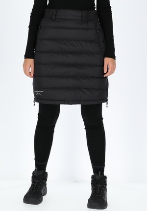 Black puffer skirt with horizontal stitching, zippered pockets, and adjustable waist; worn over black leggings and sturdy black boots.
