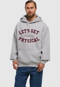 Felpa grigia con cappuccio, con testo bordeaux che recita "LET'S GET PHYSICAL Fitness Club" sulla parte anteriore. Include una tasca a marsupio.
