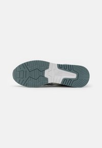Running shoe outsole in dark teal and white. Features textured tread for traction, with a distinct logo engraved on the heel.