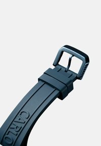 Black rubber belt featuring a sleek buckle with a textured edge. The belt is smooth with embossed logo details on the strap.