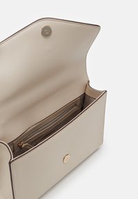 Borsa a tracolla in pelle beige con un design strutturato, apertura superiore che rivela un interno liscio, tasca con zip e dettagli in metallo dorato.