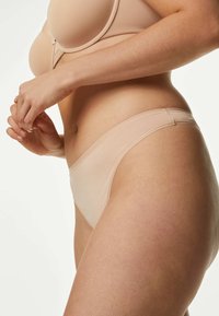 Nude stringondergoed met een gladde, lichte textuur en een elastische tailleband. Heeft naadloze zijkanten en een minimalistische dekking.