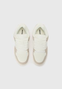 Sneakers with white leather and beige suede panels, flat white laces, perforated toe box, and printed brand name on the insoles.