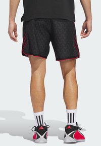 Μαύρο αθλητικό σορτς με υφή ζιγκ ζαγκ, με κόκκινες λεπτομέρειες και αντίθετο στρίφωμα. Φοριέται με άσπρες κάλτσες και μαύρα-κόκκινα παπούτσια.