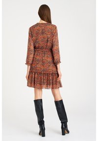 Kukallinen mekko, jossa on kootut vyötärö, kolmen neljänneksen hihat, röyhelöhelmata ja eläväinen sekoitus punaista, oranssia ja mustaa sävyä.