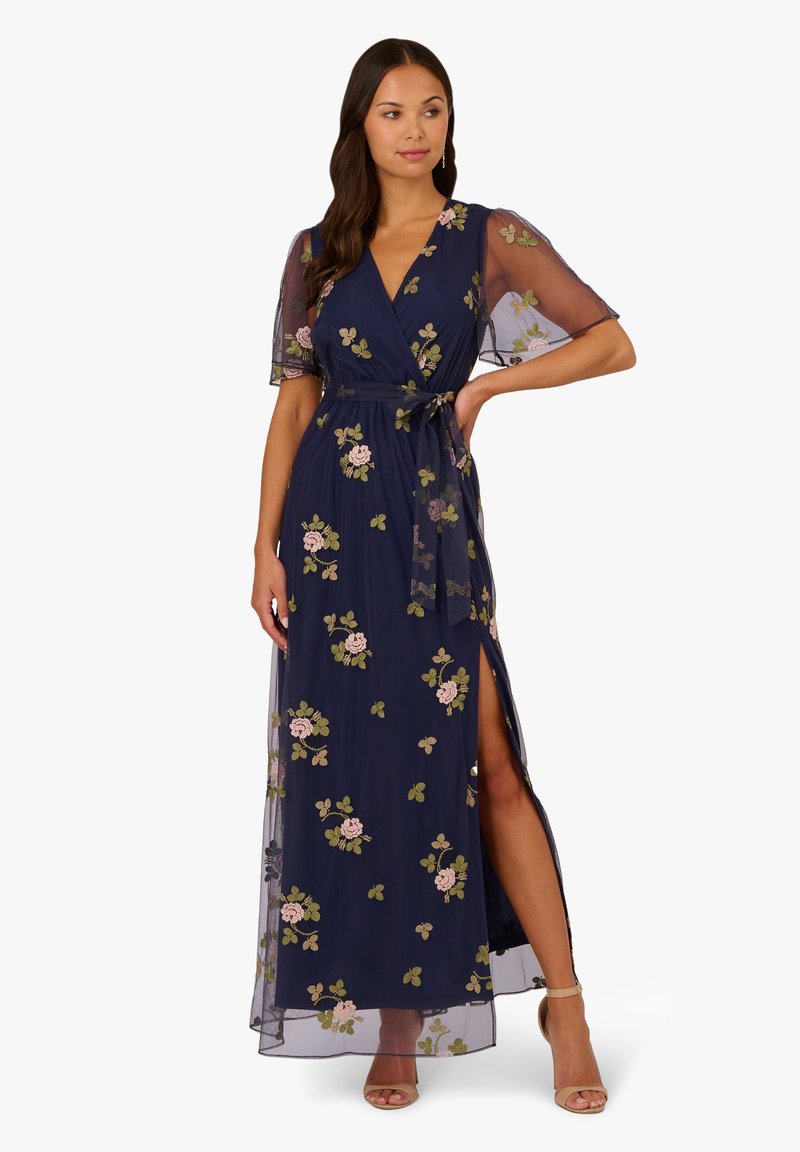 Marineblaues Wickelkleid mit transparenten Ärmeln, floralen Stickereien in Pink und Grün, Taillenknoten und einem Oberschenkel-spalt. Eleganter, leichter Stoff.