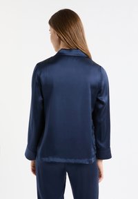 Granatowa satynowa piżama z długim rękawem, wykładanym kołnierzem i gładką teksturą. Widoczne szwy i detale krawieckie na mankietach i dole.