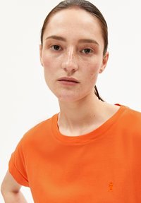 Oranges Baumwoll-T-Shirt mit Rundhalsausschnitt und kurzen Ärmeln. Verfügt über ein gesticktes Logodetail auf der Brust. Glatte Textur.