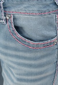 Poche en denim bleu clair avec des coutures roses et des rivets argentés ornés de décorations en pierres précieuses transparentes.