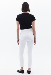 Jeans blancos ajustados de cintura alta, con bolsillos traseros. Combinados con una camiseta negra de manga corta y zapatos planos negros.