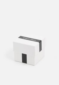 White cardboard gift box with a black stripe and "Calvin Klein" text on the lid. Square shape, clean design, no additional patterns.