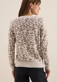 Pull en tricot beige avec un imprimé léopard brun, présentant des poignets et un ourlet côtelés. Le design est texturé et ajusté, vu d'un angle arrière.