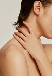 Anillo de oro con pequeñas piedras claras, distribuidas uniformemente. Se lleva en la mano, mostrando un diseño minimalista sobre la piel desnuda. Apariencia suave y delicada.