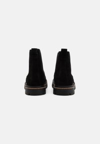 Botine negre din suede, cu vârful rotund, spatele întărit și talpă din cauciuc cu un grip texturat și cusături contrastante de culoare maro deschis.