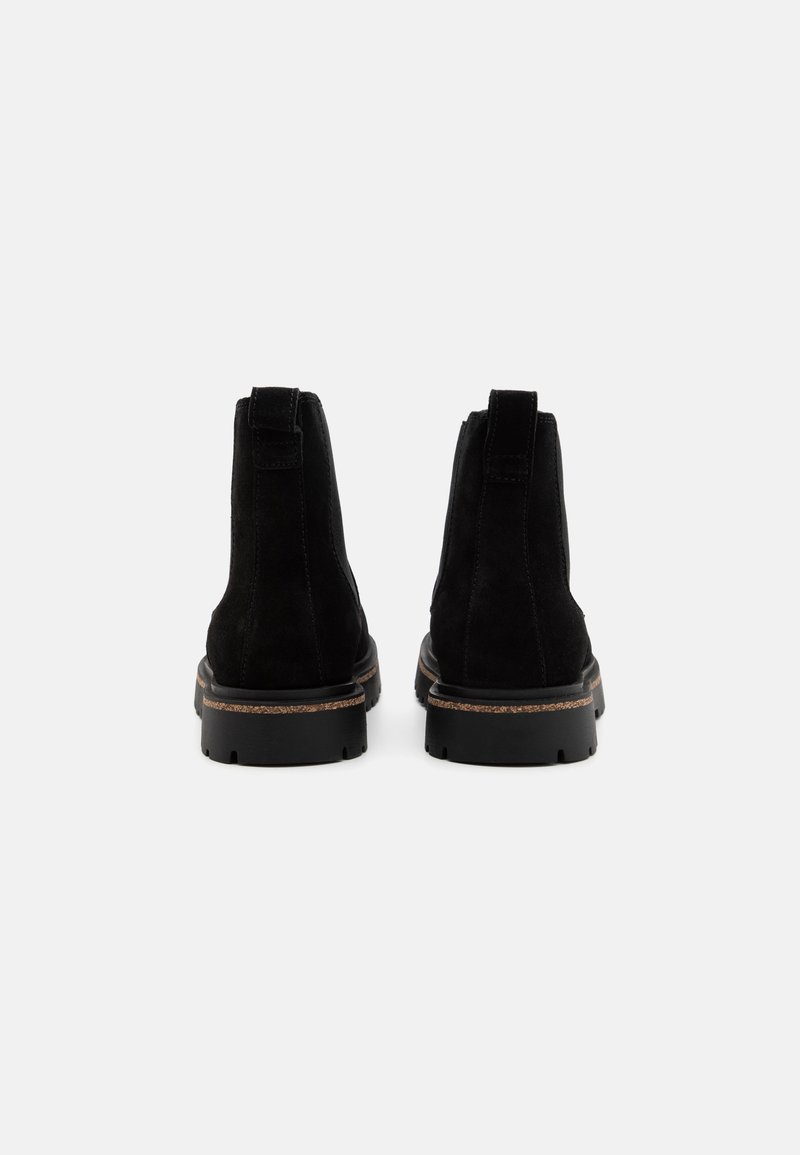 Bottines en daim noir avec un bout rond, un dos renforcé et une semelle en caoutchouc dotée d'une texture antidérapante et de coutures contrastantes en marron clair.