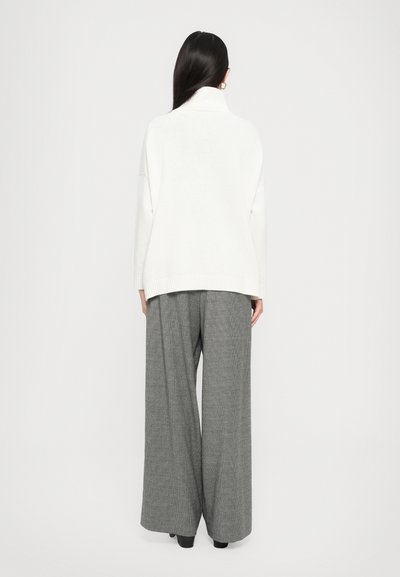 Vit stickad turtleneck-sweater med ribbade muddar och nederkant, ihopparat med grå vida rutiga byxor. Slät textur och avslappnad silhuett.