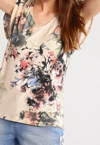 Bloemenprint top met een beige achtergrond, met tinten roze, blauw en groen. V-hals ontwerp met korte, vloeiende mouwen.