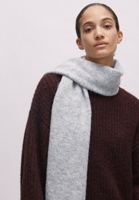 Hellgrauer Schal aus weichem, strukturierendem Material, locker um den Hals gewickelt, kombiniert mit einem dunkelburgunderfarbigen Strickpullover.