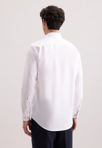 Camicia bianca a maniche lunghe con orlo curvo, polsini con bottone e design posteriore pulito, realizzata in tessuto leggero e morbido.