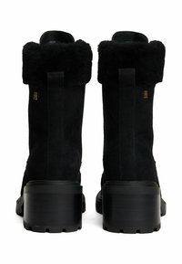 Bottines en suède noir avec un revers en fausse fourrure, dotées d'un talon épais noir et d'une semelle extérieure en caoutchouc texturé. Détail du logo doré sur le côté.