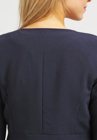 Robe bleu marine dotée d'un tissu lisse et élégant avec un dos droit et des coutures discrètes. Aucun accessoire visible ni motif.