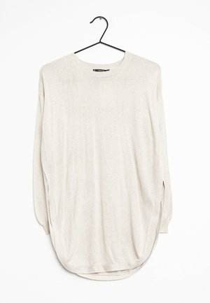 Pull beige clair à manches longues et col rond, suspendu sur un cintre noir contre un fond blanc, avec un ourlet arrondi et des fentes latérales.
