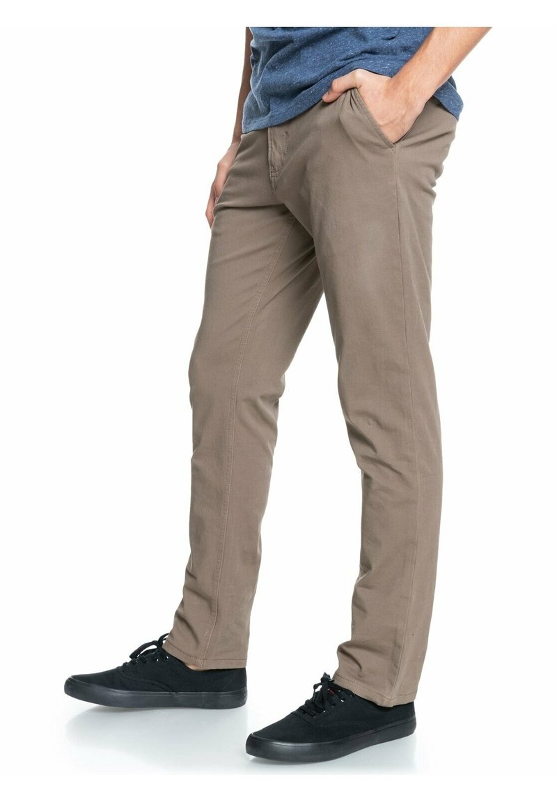 Ljust bruna stretchiga bomullbyxor med rak passform, med framfickor och en avslappnad stil, kombinerade med svarta snörskor.