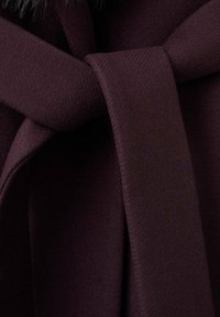 Tessuto bordò con una texture liscia, caratterizzato da un dettaglio a nodo legato. Accentuato da un componente in pelliccia nera per un maggiore interesse visivo.