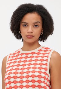 Débardeur en tricot sans manches avec motif de vagues en corail et crème, présentant une encolure ronde et un tissu texturé pour une apparence légère.