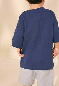 Kortärmad, blå T-shirt i avslappnad passform med rund halsringning, kombinerad med ljusgrå shorts. Tyget ser mjukt ut med en subtil struktur.