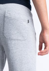 Pantalons de survêtement en coton gris avec une poche arrière, présentant un design de poche arrondi et une petite étiquette tissée sur la couture latérale.