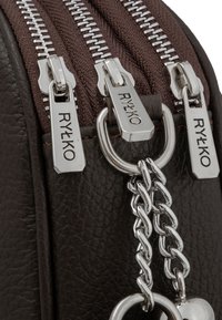 Braune, strukturierte Lederhandtasche mit silbernen Reißverschlüssen und Beschlägen. Verfügt über drei Reißverschlüsse und ein Kettenakzent mit einem herzförmigen Charme.