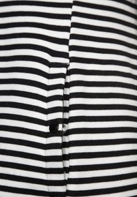 Černobíle pruhovaná látka s knoflíkovým zapínáním. Má hladkou strukturu a rovnoměrně rozložené vodorovné pruhy.