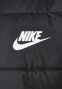 Chaqueta acolchada negra con una textura suave que presenta un destacado logo blanco de Nike y un diseño de silueta contrastante.