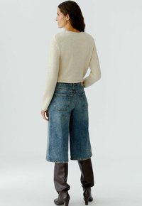 Beige cropped sweater met lange mouwen, gecombineerd met wijde blauwe denim culottes en bruin leren laarzen tot aan de knie.