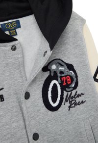 Felpa grigia con cappuccio nero, caratterizzata da un design ricamato di moto e testo "Motor Race". Bottoni a pressione e texture morbida.