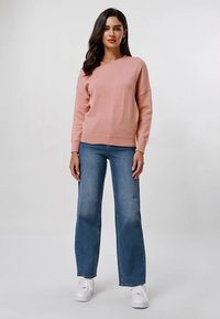 Un pull surdimensionné rose avec un décolleté en V, associé à un jean taille haute bleu clair à jambes larges et des baskets blanches.