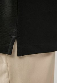 Zwarte stoffen top met zijinsnijdingen, gestructureerde afwerking en een nette zoom, gecombineerd met beige broekstof met diagonale lijnen.
