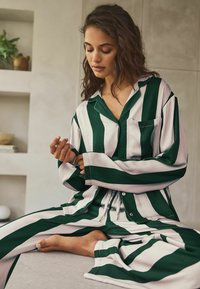 Pyjama rayé vert et blanc avec une coupe décontractée, comprenant une chemise à boutons et une taille élastiquée, fabriqué en tissu doux.