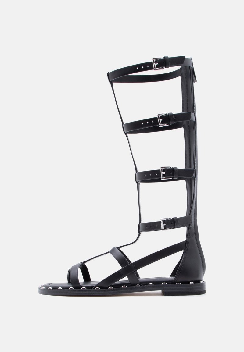 Μαύρο γυναικείο σανδάλι τύπου γκλαδιέτορα μέχρι το γόνατο με πολλαπλούς ιμάντες ρυθμιζόμενους με αγκράφες και λεπτομέρειες με ασημένια καρφιά κατά μήκος της άκρης της σόλας.