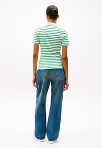 Πράσινη και λευκή ρίγα μπλούζα με κοντά μανίκια, συνδυασμένη με φαρδύ τζιν παντελόνι σε μπλε απόχρωση. Λείο ύφασμα, ψηλή μέση και φαρδιά γραμμή.