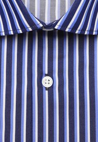 Gros plan d'une chemise rayée verticalement bleu, blanc et noir avec un col et un seul bouton blanc fermé au centre.