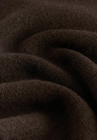 Braun gestrickter Stoff mit einer weichen, strukturierten Oberfläche, die sanfte Kurven und Falten aufweist, die Tiefe und Dimension erzeugen.