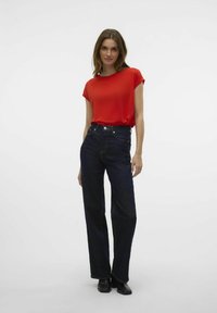 T-shirt rouge à manches courtes associé à un jean droit taille haute bleu marine. Des boots noires à la cheville complètent la tenue. Design minimaliste.