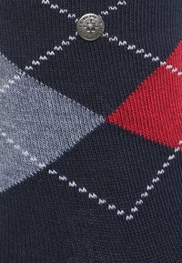 Calzino blu navy con motivo argyle composto da diamanti rossi, grigi e bianchi. Include un bottone con logo argentato come dettaglio. Tessuto a maglia testurizzato.