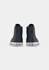 Sneakers înalți de culoare bleumarin cu talpă din cauciuc alb, prezentând un material texturat și cusături în contrast. Brandul Converse All Star pe toc.