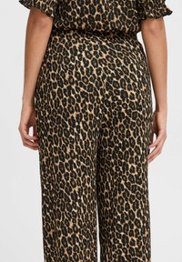 Pantalons évasés imprimé léopard en tissu texturé noir et beige, avec une taille haute et un détail froncé en haut.
