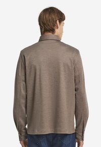 Brun skjorta med krage och långa ärmar, mjuk textur, bakifrån med knäppta manschetter och rak skärning i nederkant.