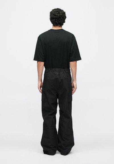 Juodas medvilninis marškinėliai su trumpomis rankovėmis, derinami su juodomis krovinių kelnėmis, pasižyminčiomis laisvu siluetu, elastinga juosmens juosta ir šoninėmis kišenėmis.