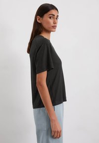 Zwarte t-shirt met korte mouwen, ontspannen pasvorm en ronde hals, gemaakt van zachte stof. Gekocht met lichtblauwe broek, weergegeven in profiel.